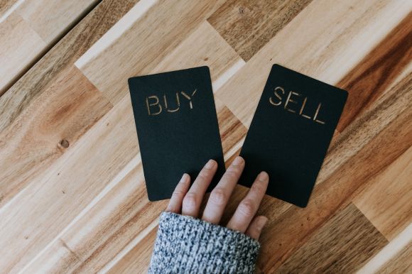 Coinbase - a person holding two small black books with the words buy and sell on them
