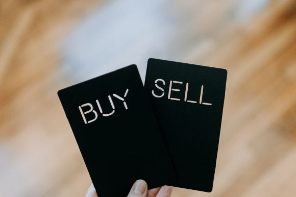 Coinbase - a hand holding two black cards with the words buy and sell written on them